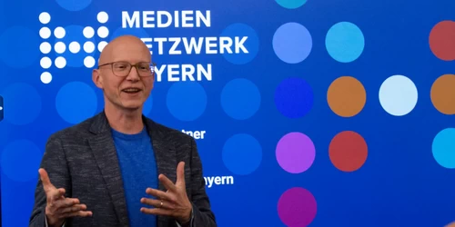 Referierender vor Logo mit Mediennetzwerk Bayern